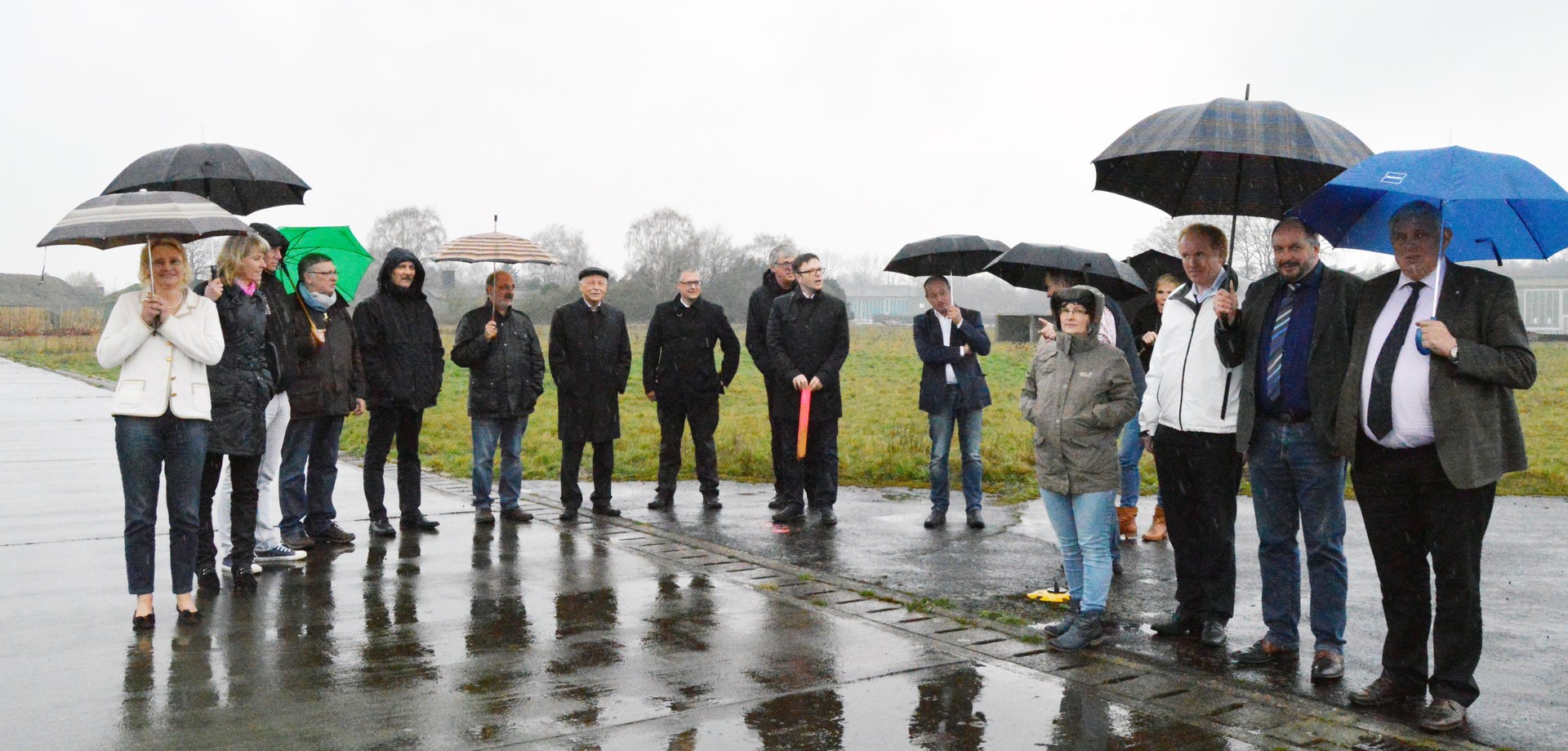 Eine Gruppe von Menschen steht mit geöffneten Regenschirmen auf der regennassen ehemaligen Landebahn