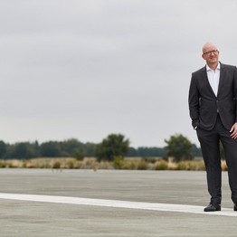 Tilmann Hollweg steht auf dem Rollfeld des ehemaligen Nato-Flugplatzes Hopsten. Er trägt einen Anzug und ein weißes Hemd und schaut in den Himmel.